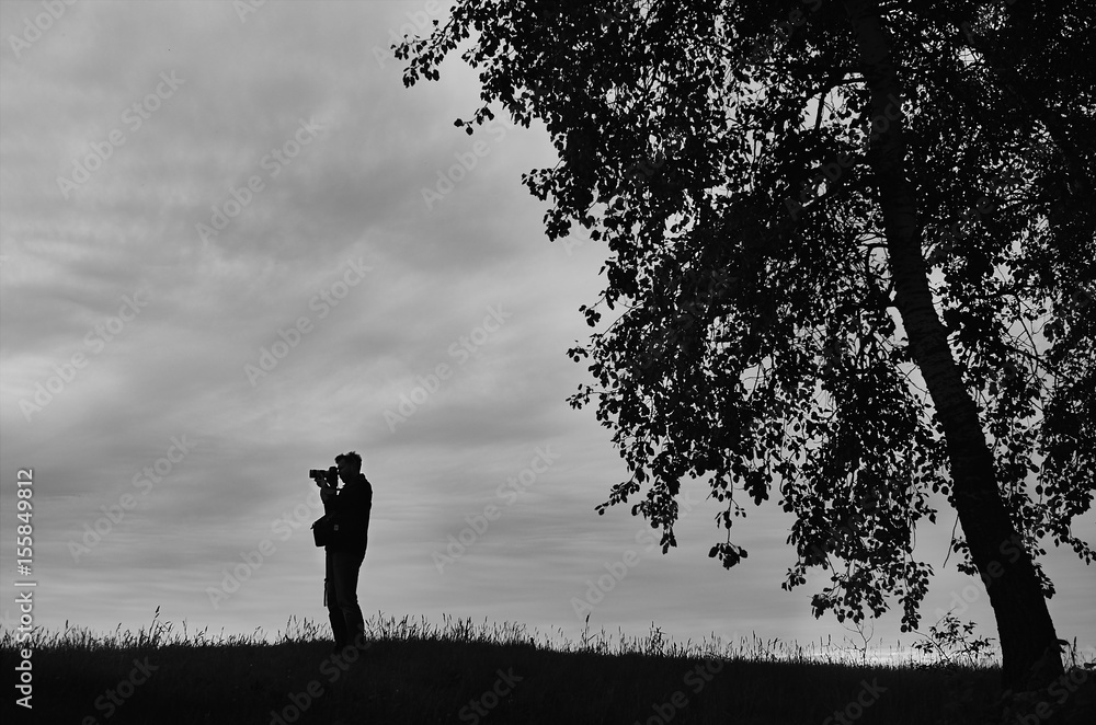 Silhouette of a photographer in a field near a tree Silhouette of a photographer in a field near a tree