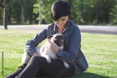 portrait of young woman and pug having god time in the park on green grass during sunset or sunrise 