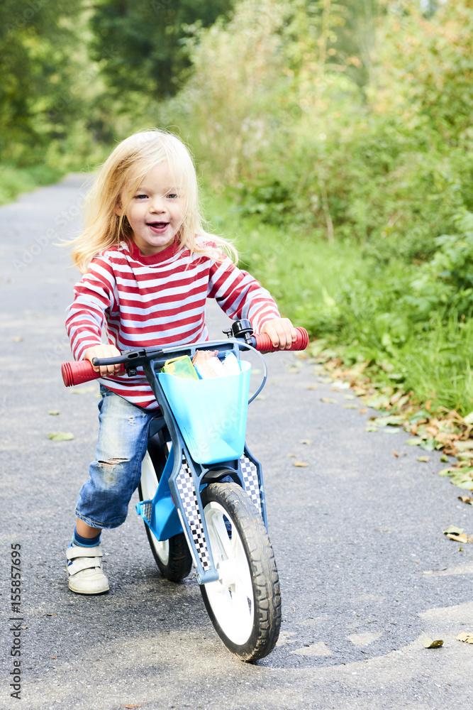 Child riding balance bike. Kid on bicycle in sunny park. Little girl ride glider bike on warm summer day. Preschooler learning to balance on run bicycle. Sport for kids Child riding balance bike. Kid on bicycle in sunny park. Little girl ride glider bike on warm summer day. Preschooler learning to balance on run bicycle. Sport for kids