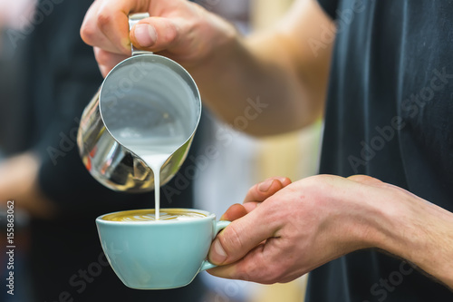 Barista in coffee bar preparing proper cappuccino pouring frothed milk into cup of coffee, making latte art, pattern creation. Professional service, catering concept