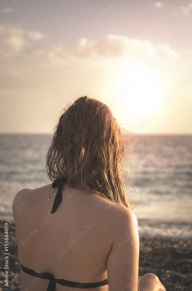 A young woman with wet hair at the beach on a background of sea sunset