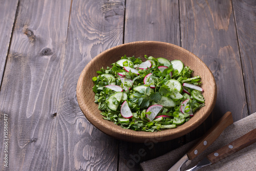 Vitamin salad of wild herbs with cucumber, radish and green onions in a wooden bowl on a wooden background. Healthy detox diet food