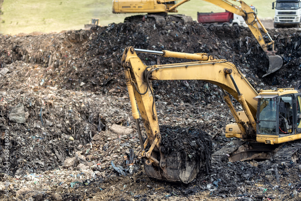 Monster industrial excavator digging into trash at urban dumping grounds