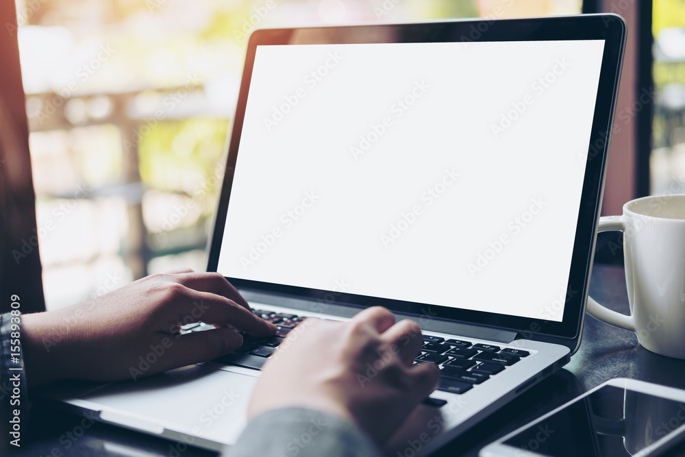Mockup image of business woman using and typing on laptop with blank white screen and coffee cup on glass table in modern loft cafe Mockup image of business woman using and typing on laptop with blank white screen and coffee cup on glass table in modern loft cafe