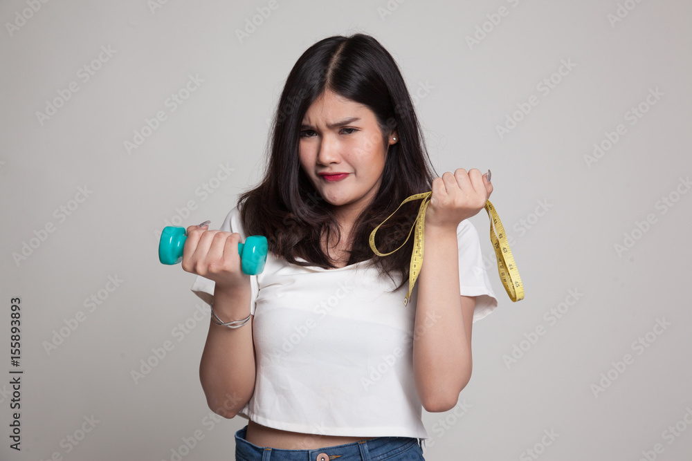 Exhausted Asian woman with dumbbells and measuring tape. Exhausted Asian woman with dumbbells and measuring tape.