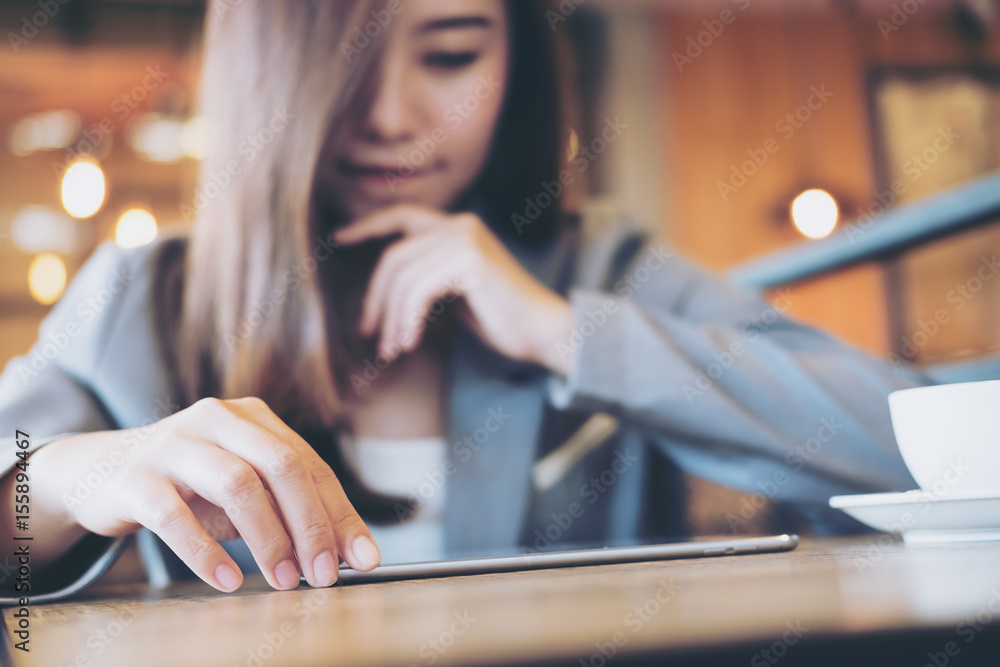 An Asian business woman thinking and using tablet with blur background in cafe An Asian business woman thinking and using tablet with blur background in cafe