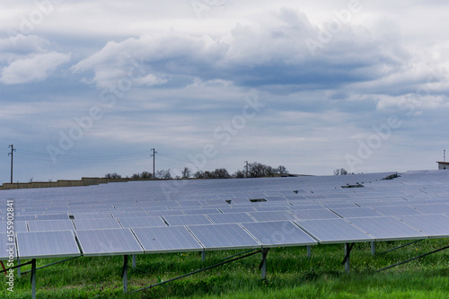 Close plan of a solar plantation panels  a green meadow and a beautiful cloudy sky  copy space. Concept energy.