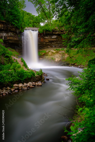 A flowing Minnehaha Falls framed by green trees at dusk
