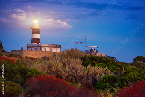 Lighthouse at sunset surrounded in the Mediterranean vegetation composed of multicolored bushes