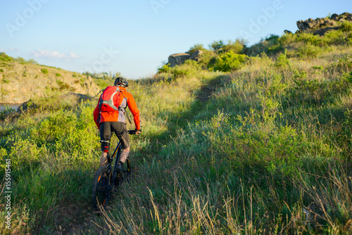 Cyclist in Red Jacket Riding Mountain Bike on the Beautiful Spring Trail. Travel and Adventure Sport Concept