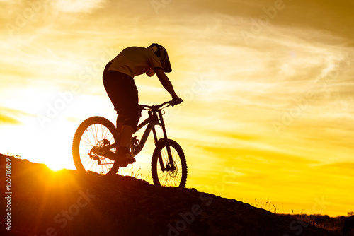 Silhouette of Cyclist Riding Down the Mountain Bike on Rocky Hill at Sunset. Extreme Sport Concept.