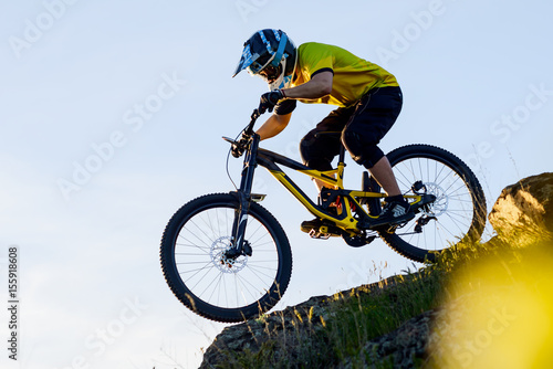 Fototapeta Naklejka Na Ścianę i Meble -  Cyclist in Yellow T-shirt and Helmet Riding the Mountain Bike Down Rocky Hill. Extreme Sport Concept.