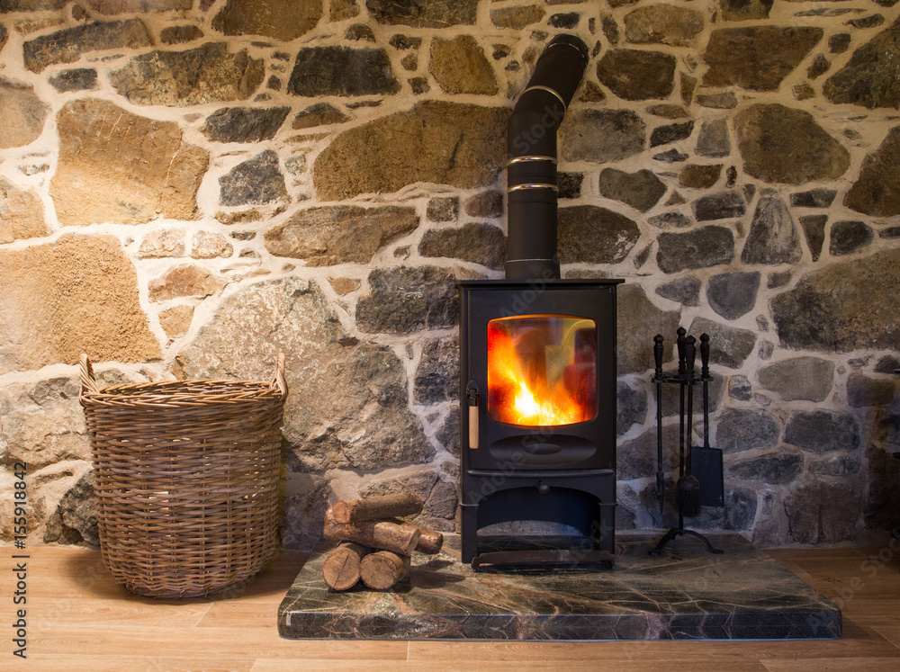 The interior of a cosy, stone cottage with stone walls and a fireplace with logs  burning in a wood burner on a fireplace and hearth. Stock-Foto | Adobe Stock