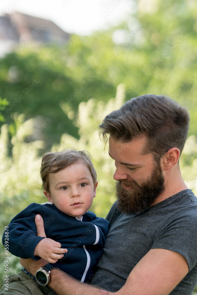 Young hipster father holding his little son in park Young hipster father holding his little son in park