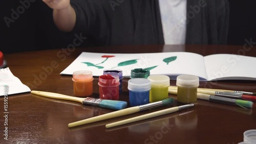 Kid artist girl painting in white drawing album, painter workplace with gouache ink jars photo