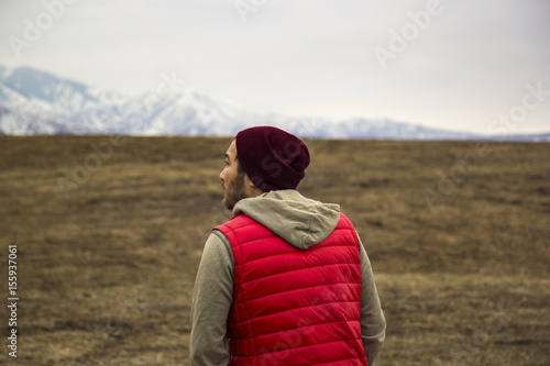 lonely man in red waistcoat walking toward mountains background © tache
