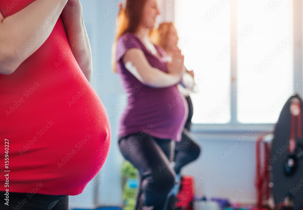 Pregnant women in a row meditating in lotus pose at yoga class