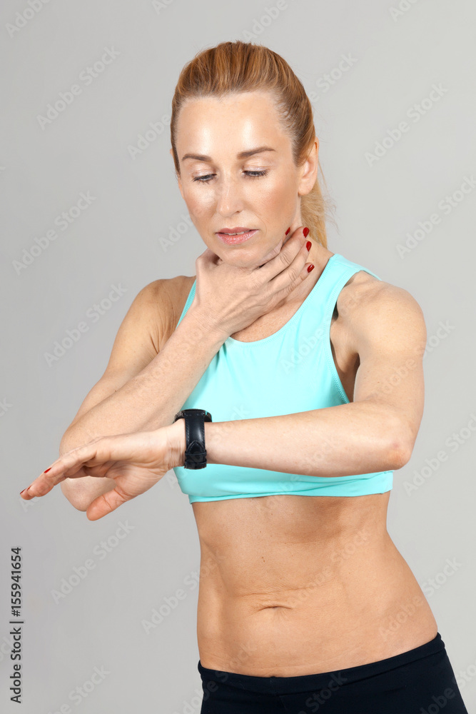 Fototapeta premium middle-aged athletic woman taking his pulse rate on the grey background