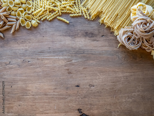 Various mix of dry pasta on wooden rustic table. Top view.