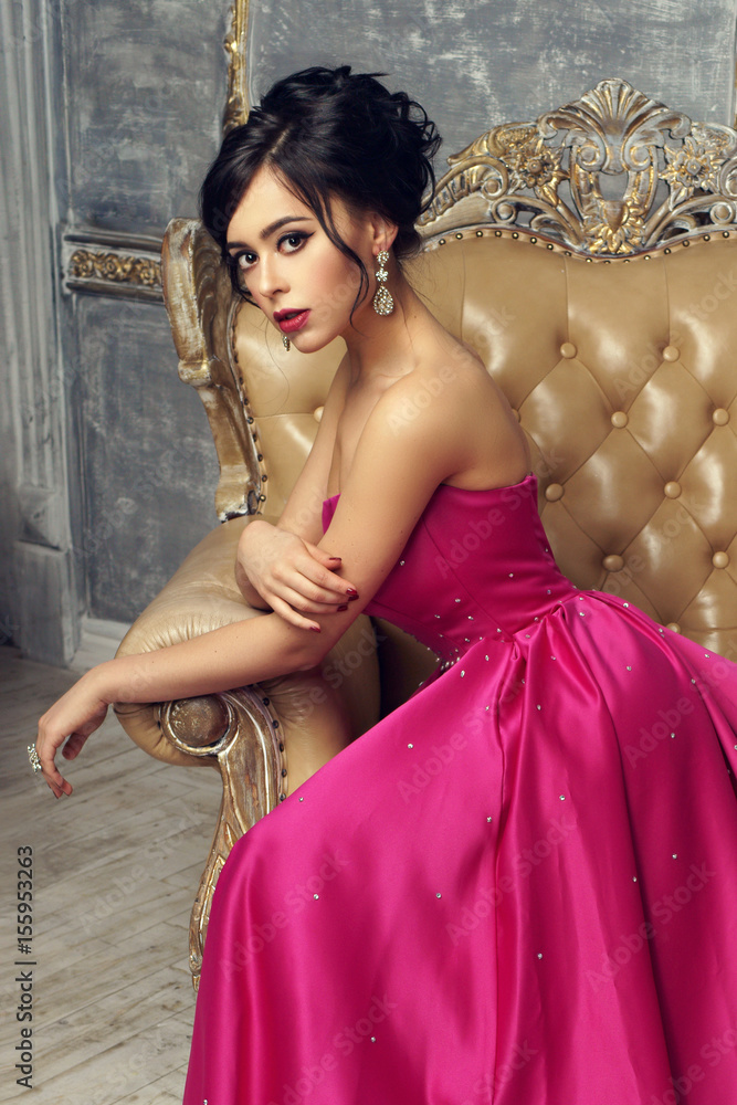 Elegant srunning woman sitting in armchair and looking at you. Pretty lady  with hairstyle wearing pink ball gown or evening dress. Stock Photo | Adobe  Stock