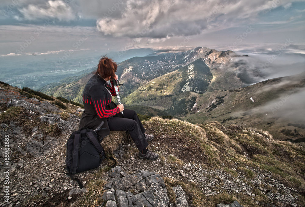 Rear view of a woman sitting on a mountain top peacefully gazing at low-lying  clouds. HDR image.