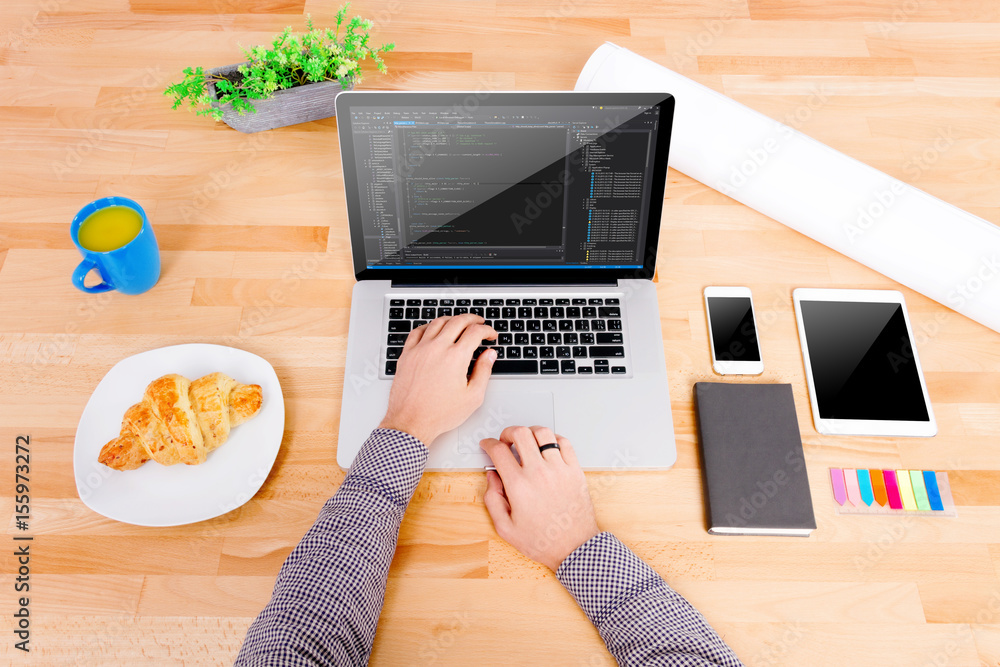 Software engineer's workplace with laptop, tablet, mockup smartphone, blue  cup, croissant. The engineer working on the laptop. Note: Code was got from  github with free license for commercial use (MIT) Stock Photo