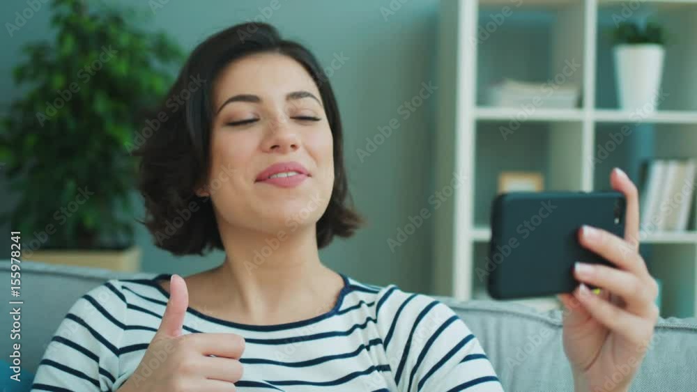 Young woman having video call with her friend on her mobile smartphone while sitting on the couch at home. Close up