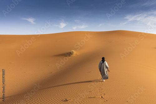 Berber man walking on the sand dunes of Erg Chebby, Merzouga, Morocco photo