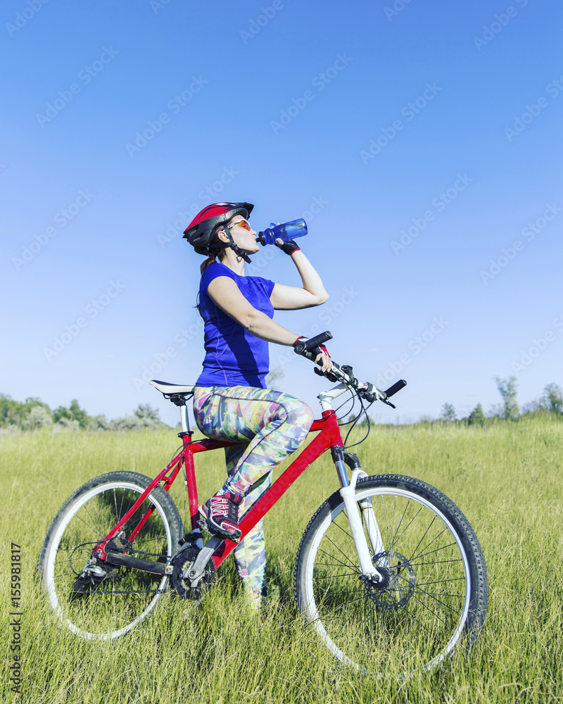 Attractive, healthy woman drinks from her water bottle on mountain bike. active outdoor lifestyle concept.