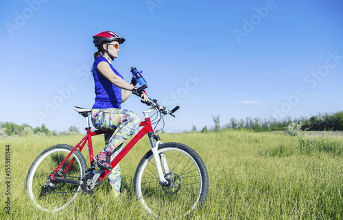 Attractive, healthy woman drinks from her water bottle on mountain bike. active outdoor lifestyle concept.
