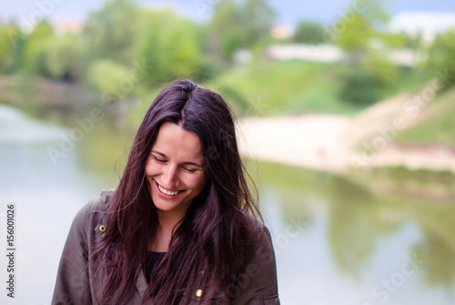 A beautiful girl without makeup with long dark hair laughing near the river.