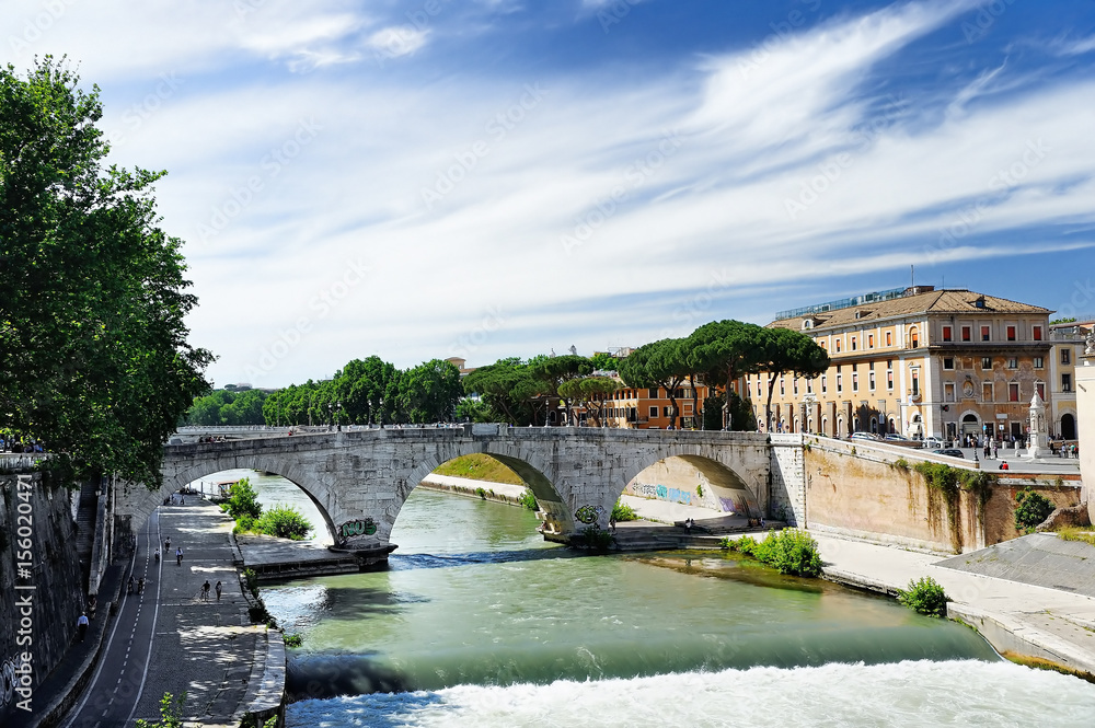 View of Tiber Island across Tiber River with ancient Roman stone bridge Pons Cestius in Rome, Italy View of Tiber Island across Tiber River with ancient Roman stone bridge Pons Cestius in Rome, Italy