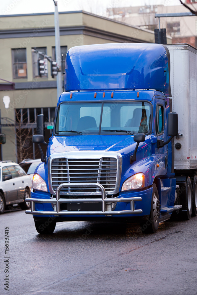 Modern bright blue semi truck with trailer and bumper Protection on city street Modern bright blue semi truck with trailer and bumper Protection on city street