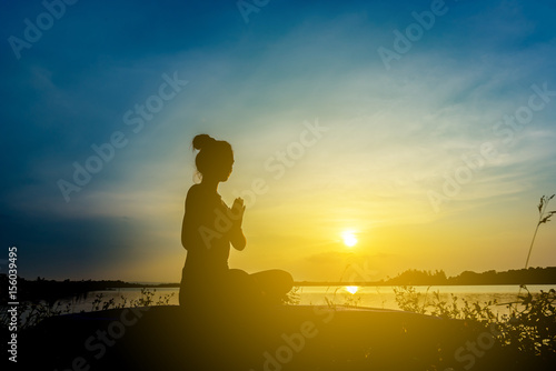 Silhouette beautiful women yoga in nature on the rock and river over sunset background.