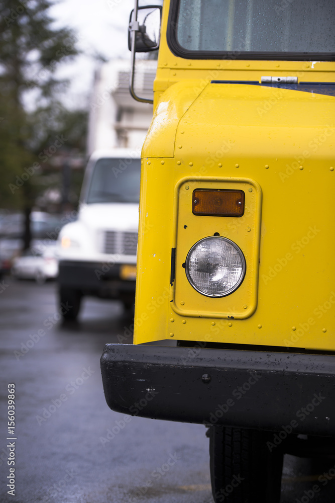 Yellow delivery box truck with headlightand semi truck on background