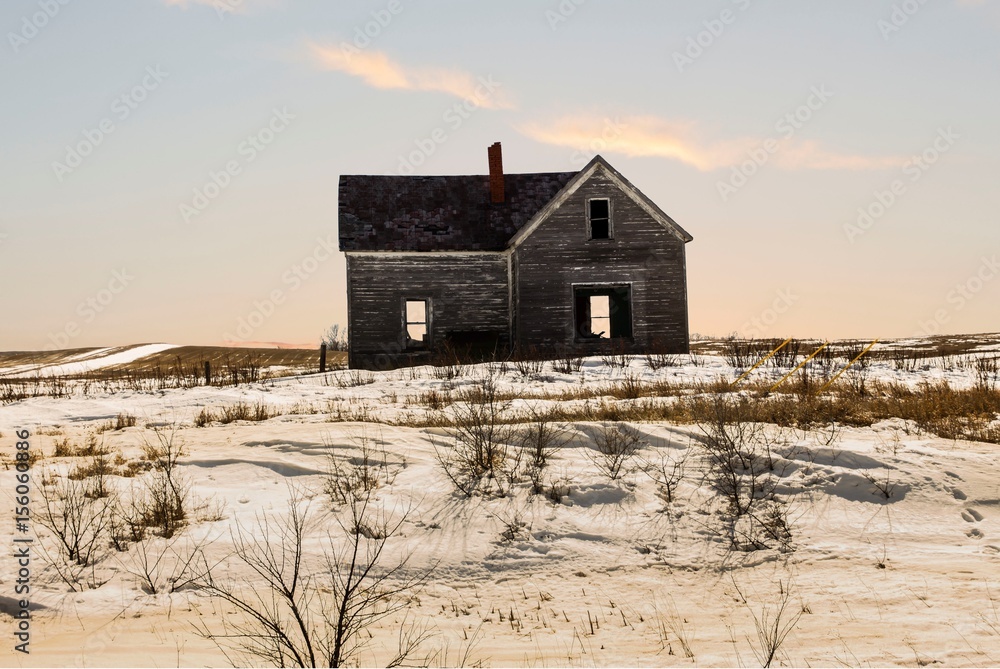horizontal image of an old abandoned house with dead grass and snow all around with the sun starting to set in the early evening. horizontal image of an old abandoned house with dead grass and snow all around with the sun starting to set in the early evening.