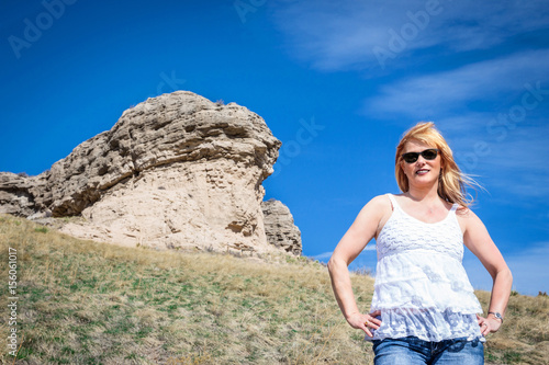 horizontal image of the top half torso of a caucasian female model with reddish blonde hair posing in front of a large rock cliff in the summer