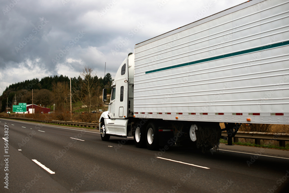Big modern white semi truck trailer reefer on wide highway