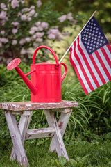 Red watering can with American flag on shabby white potting bench in garden