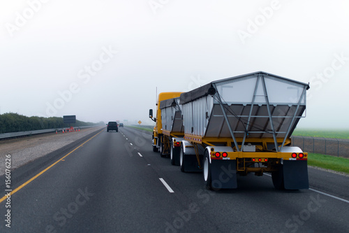 Chic new yellow truck with two bulk trailers on straight as arrow highway in fog