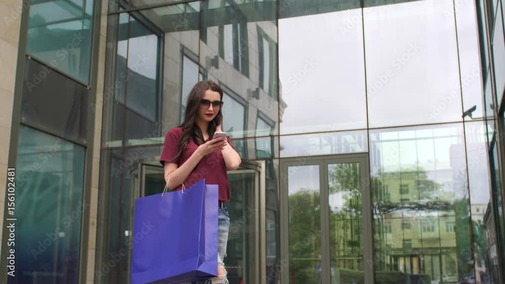 Beautiful young fashion woman with shopping bags and phone standing near shop window. Beautiful young fashion woman with shopping bags and phone standing near shop window.