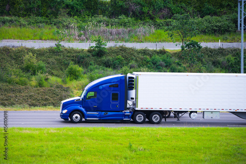 Φωτογραφία Modern dark blue semi truck reefer trailer profile on green road