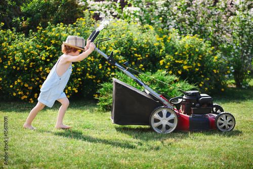 little boy mows lawn with mower