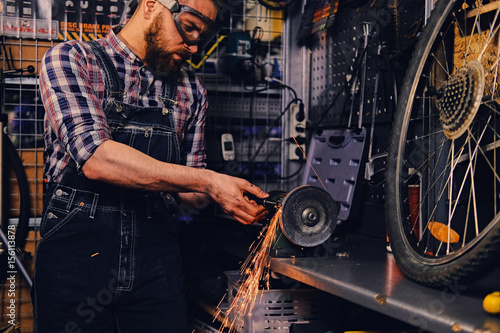 Bearded mechanic fixing bicycle's wheel in a workshop.