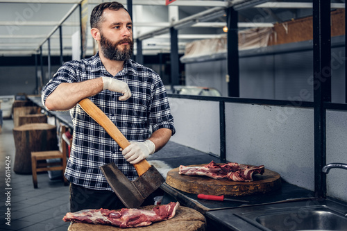 Portrait of a butcher holds an axe and fresh cut meat.