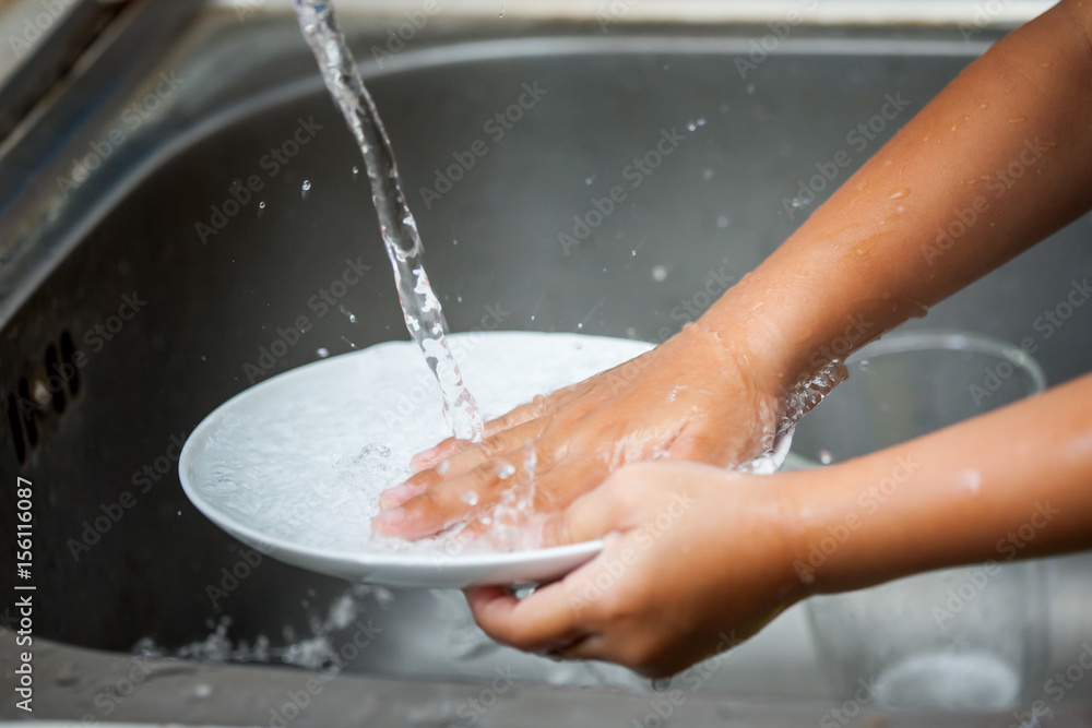 Fototapeta premium Child hand washing dishes over the sink in the kitchen