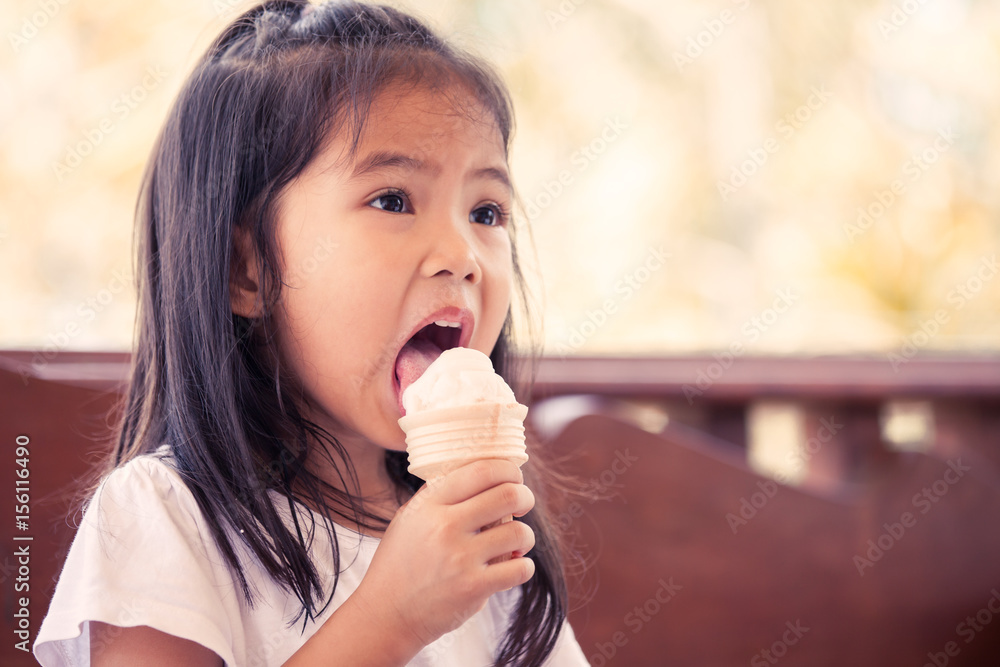 Cute asian little girl is eating ice cream cone in vintage color tone Cute asian little girl is eating ice cream cone in vintage color tone