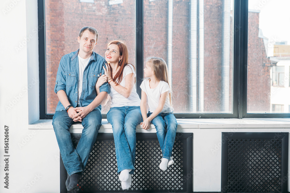 Happy family mother father child portrait sitting on window sill Happy family mother father child portrait sitting on window sill