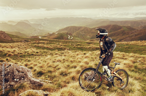 Downhill rider on a mountain bike in a mountain bike rides along the road in nature against the backdrop of the mountain range of mountains and rainy skiesExtreme Sport Concept.