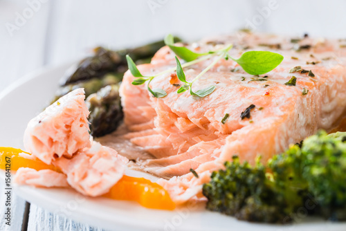 Baked salmon with vegetables on plate. White wooden table